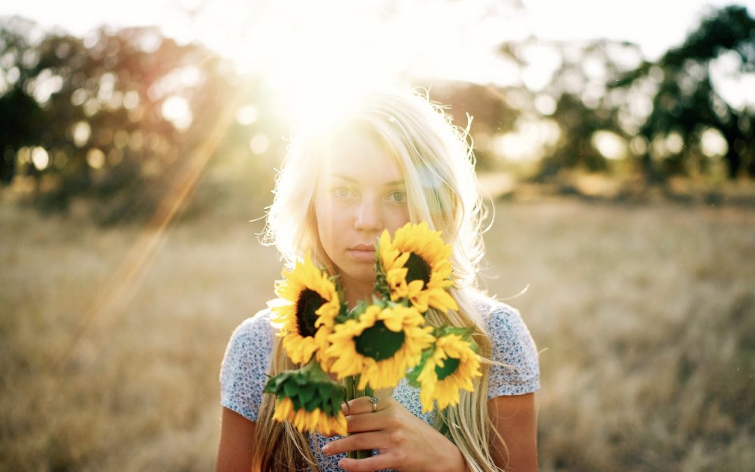 A young woman holding healthy sunflowers in a field.